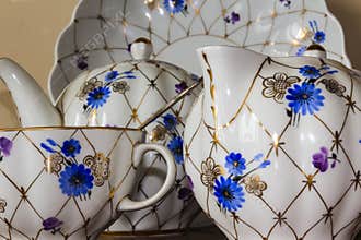 Porcelain sugar bowl, cup, milk, dish with golden pattern and blue flowers.