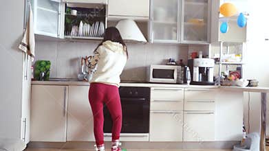 Joyful young beautiful woman is dancing in kitchen wearing pajamas and headphones drinks a cup of coffee in the morning