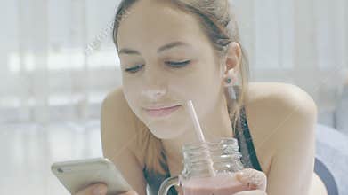Young woman is drinking a smoothies and using a fitness app on her smartphone.