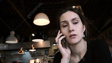 Young beautiful woman sitting in cafe and talking on mobile phone. Attractive female uses smartphone for work.