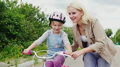 The first successes of children. A woman teaches her daughter to ride a bicycle, applauds her success