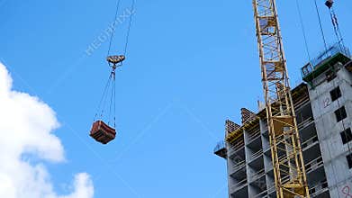Crane and building construction site against blue sky. heavy load hanging on the hook of a crane on the construction of