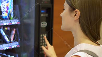 Beautiful hungry woman picking item out of vending machine in mall. Choosing unhealthy snacks being hungry