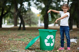 A little child putting the garbage in a green recycling bin on a blurred natural background. Ecology pollution concept.