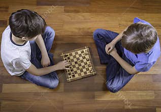 Kids playing chess sitting on wooden floor. Top view. Game, education, lifestyle, leisure concept