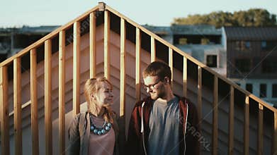 Young beautiful couple standing on the roof and enjoying the scenic view on sunset. Romantic date of man and woman.