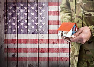 Close up of soldier holding a little house in front of american flag