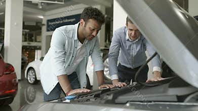 The seller shows the motor of modern auto to a buyer in car showroom