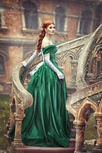 Beautiful, young, red-haired girl in a green medieval dress, climbs the stairs to the castle. Fantastic photosession.