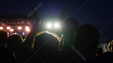 Woman jump with hands up at rock festival, colourful lights on stage, colorful lighting during night rock concert