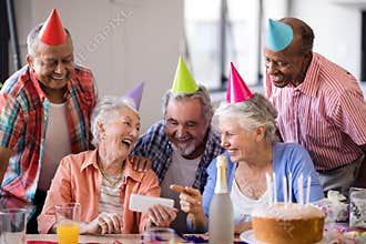 Cheerful senior woman showing mobile phone to friends in party