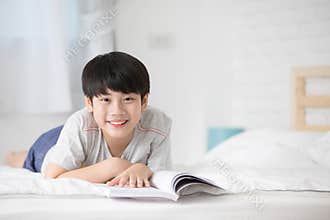 Happy Asian boy reading story book on the bed