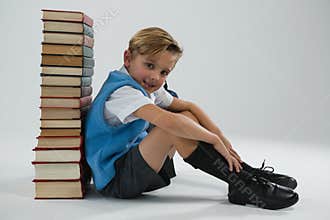 Schoolboy sitting against books stack on white background