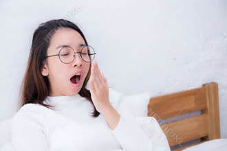Beautiful asian woman waking up and yawn in bed in the bedroom.