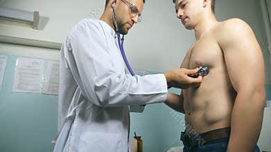 Doctor examining young male patient with stethoscope. Medic checking chest of guy in her office at the hospital. Medical