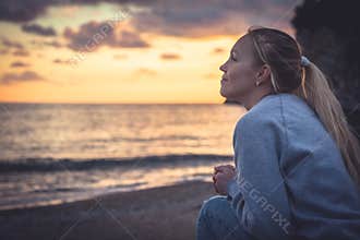 Pensive lonely smiling woman looking with hope into horizon during sunset at beach