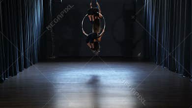 Flexible girls makes a gymnastic elements on the aerial hoop