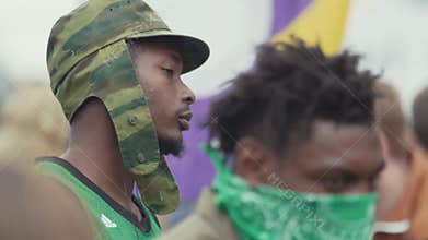 Two pensive young black gangster guys sitting at crowded outdoor event