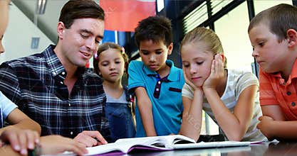 Kids listening to teacher while reading book in classroom