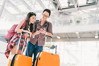 Asian couple travelers using smartphone checking flight or online check-in at airport, with passport and luggage