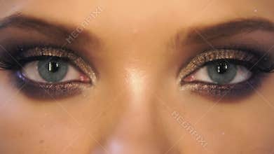 Closeup view of woman`s eyes with beautiful golden makeup opening and closing in slowmotion