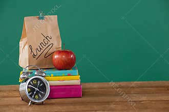 Alarm clock, lunch paper bag and apple on books stack