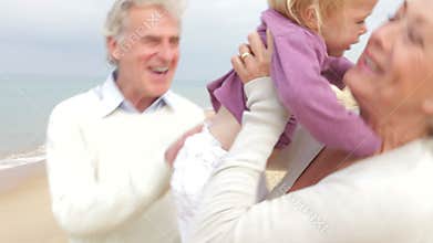 Grandparents And Granddaughter Walking Along Beach Together