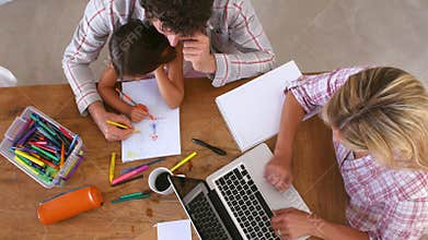 Overhead View Of Family Coloring Picture And Using Laptop