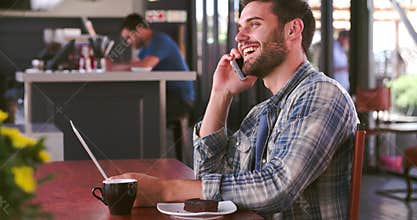 Man In Cafe Working On Laptop And Answering Phone