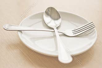 Plate isolate with spoon and fork on a wooden table . (Focus at