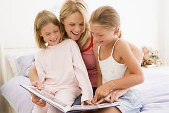 Woman and two young girls in bedroom reading book