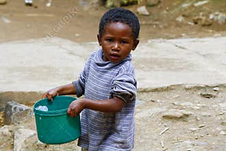Poor malagasy boy carrying plastic water bucket