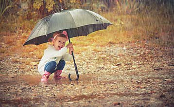 Happy baby girl with an umbrella in the rain playing on nature