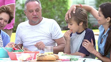Multi Generation Family Enjoying Meal In Garden Together