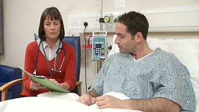 Doctor Sitting At Male Patient's Bedside Having Discussion