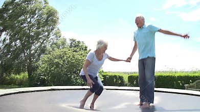 Senior Couple Bouncing On Trampoline In Slow Motion