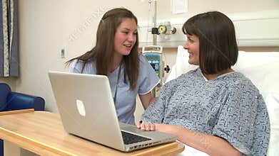Nurse Sitting By Female Patient's Bed In Hospital