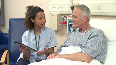 Nurse Sitting By Male Patient's Bed Using Digital Tablet