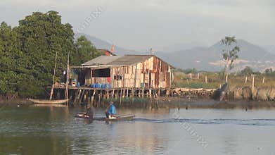 Boat floating on river near the house on stilts.Two fishermen sit in the boat.