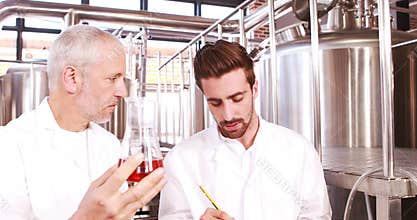 Two men in lab coat looking at the beaker with beer