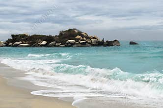 Tiny rocky isle close to sandy beach and foamy waves in turquoise sea