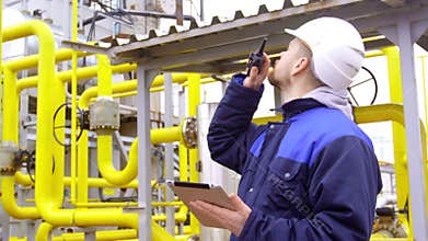 Engineer holding a tablet, talking on walkie-talkie in modern industrial factory