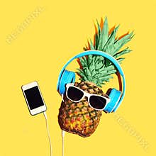 Fashion pineapple with sunglasses and headphones listens music on smartphone over yellow background