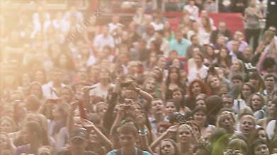 View of cheering people at summer live concert. Music band performing on stage. Crowd. Sun beams