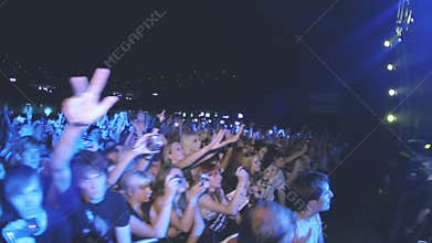 People sway hands on live rock concert in nightclub. Band performing on stage. Spotlights.