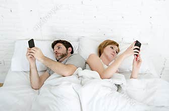 young couple using mobile phone in bed ignoring each other in relationship communication problems