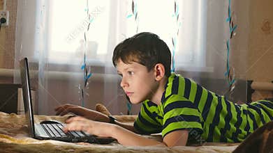 Boy laptop browsing internet is playing lying in bed