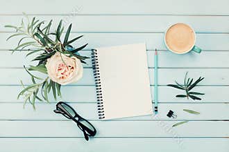 Morning coffee cup, clean notebook, pencil, eyeglasses and vintage rose flower in vase on blue rustic table top view. Flat lay.