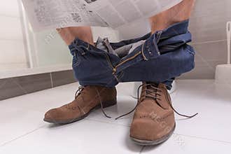 Adult male wearing jeans and shoes reading newspaper while sitti