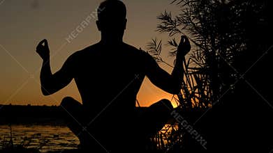 Silhouette of young man practicing yoga on the beach at sunset. 4K